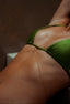 Green bikini top with gold chain worn by a person with a blurred background