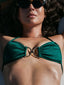 Woman wearing a green bikini top with a gold clasp, sunbathing outdoors.
